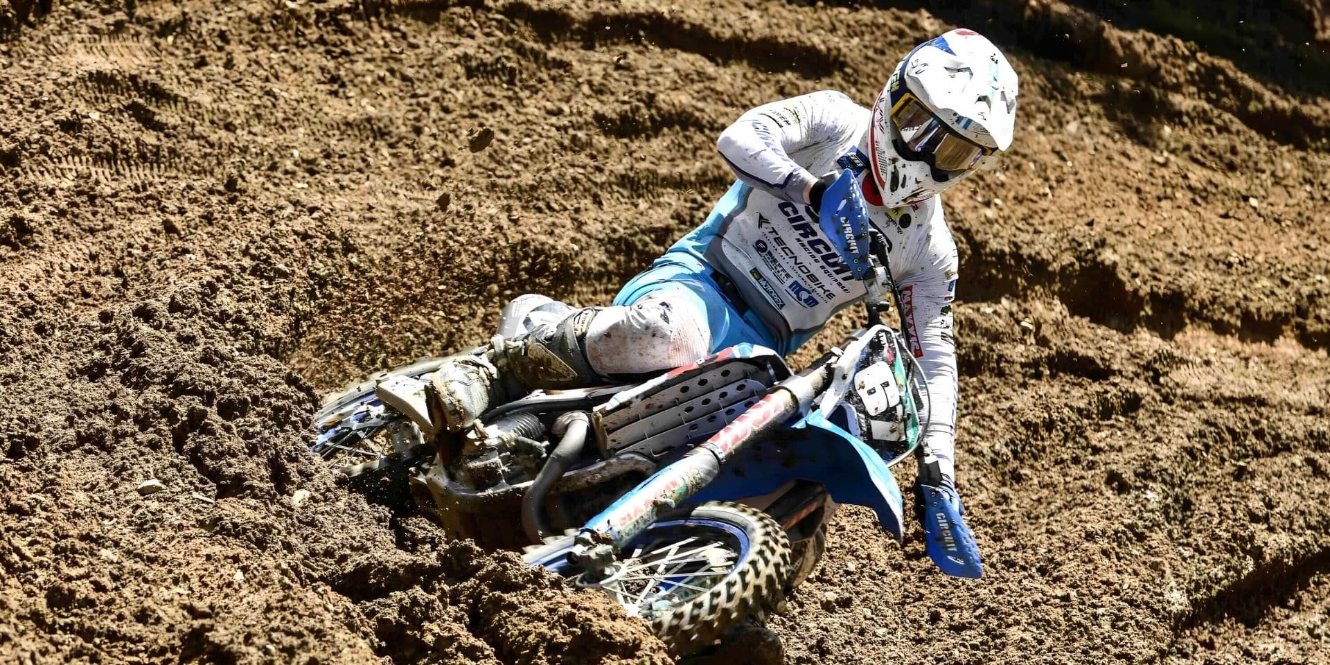 Pilote TM Moto en pleine accélération dans un virage de motocross sur terrain sableux